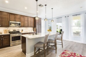 Una cocina con armarios de madera, electrodomésticos de acero inoxidable, encimera de granito e iluminación colgante.