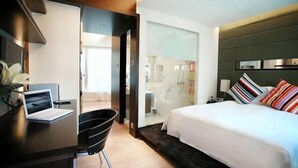 A modern hotel room with a bed, a desk, and a chair. There is a glass door leading to a bathroom. - Knight On Wyndham (Hong Kong)