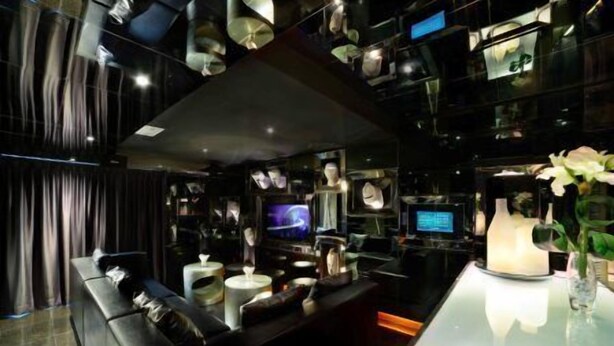 A modern interior with a dark color scheme, featuring a sofa, a table with a vase, and a television. - Knight On Wyndham (Hong Kong)