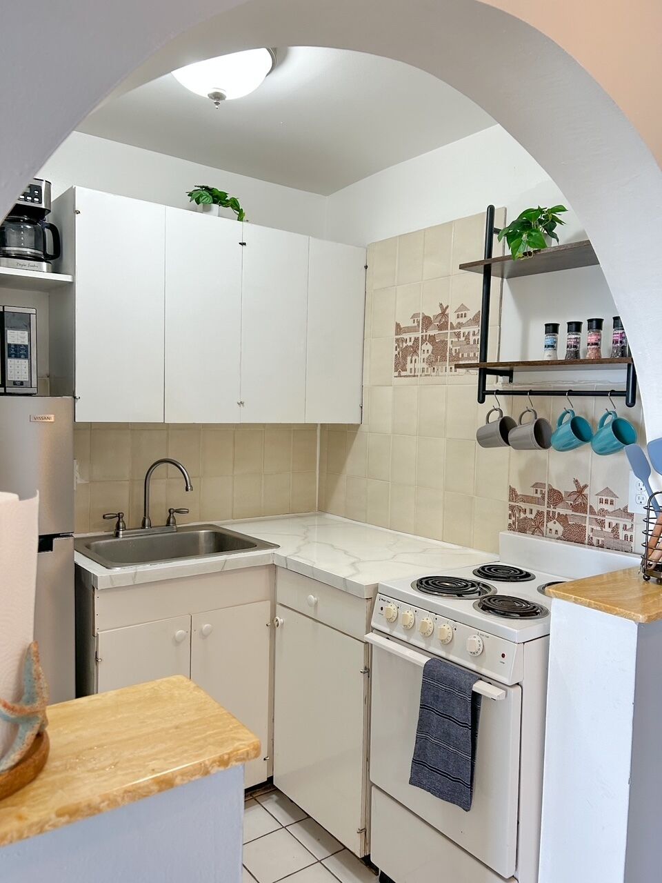 Une cuisine compacte avec des meubles blancs, une cuisinière encastrée, un évier et une machine à café.