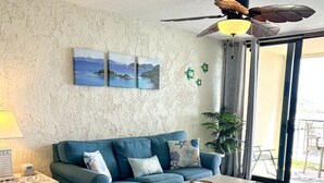 Ein Wohnzimmer mit einem blauen Sofa, einem Holztisch, einem Deckenventilator und Blick ins Freie.
