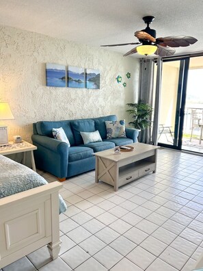 A living room with a blue sofa, a wooden coffee table, a ceiling fan, and a view of the outdoors. - Romantic Oceanview Escape -- Private Balcony Views -- Close to Sapphire Beach (Sapphire Village)