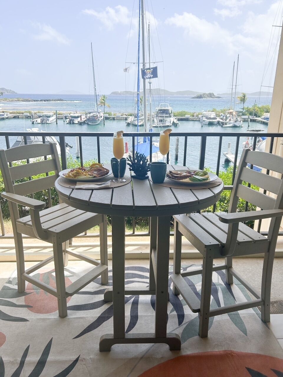 A round table with chairs on a balcony overlooking a marina with boats and a distant island.