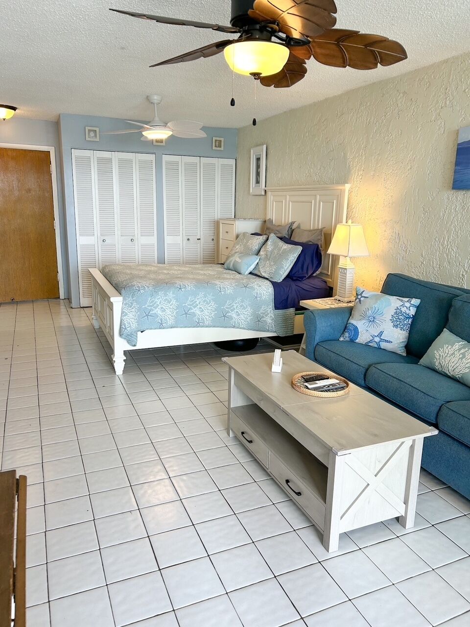 A bedroom with a bed, a nightstand, a lamp, a sofa, and a ceiling fan.