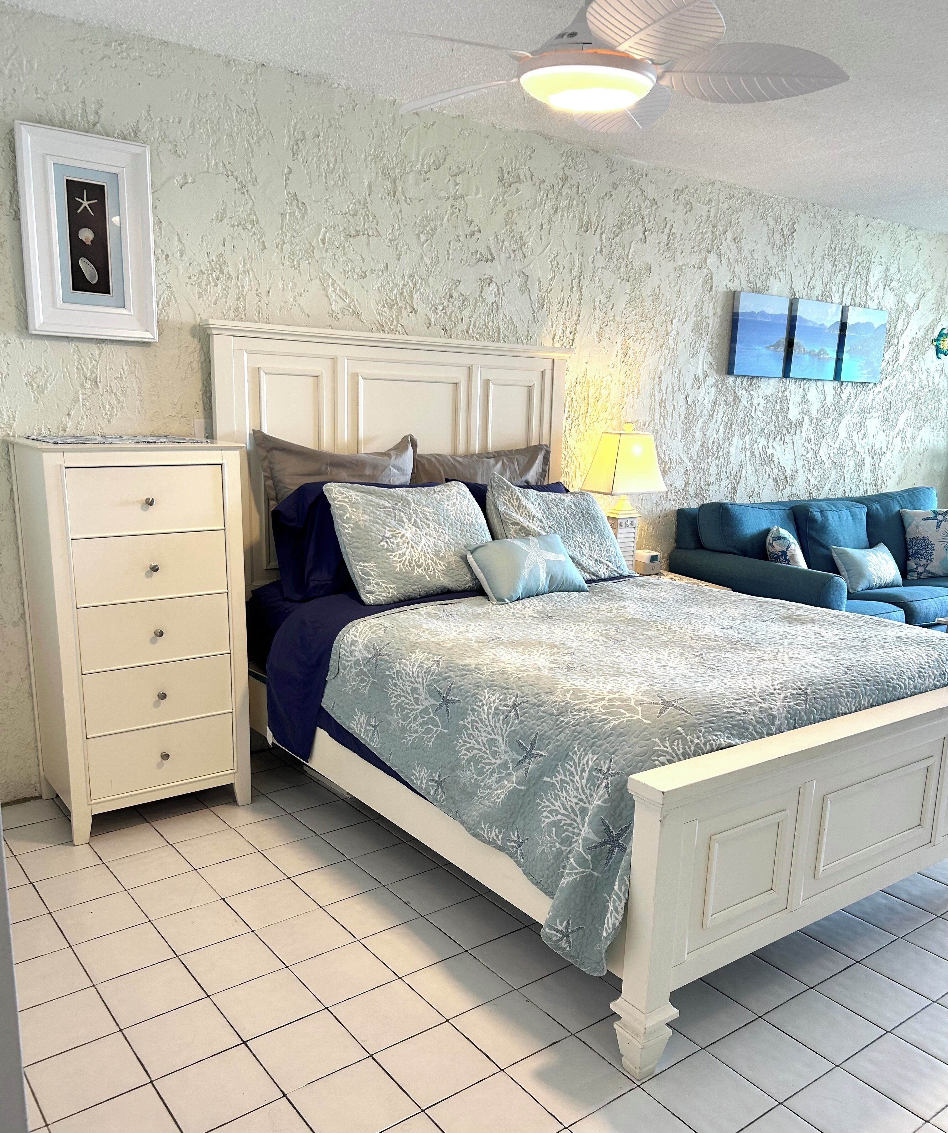 Ein Schlafzimmer mit einem Bett, einem Schminktisch, einem Nachttisch und einem Deckenventilator.