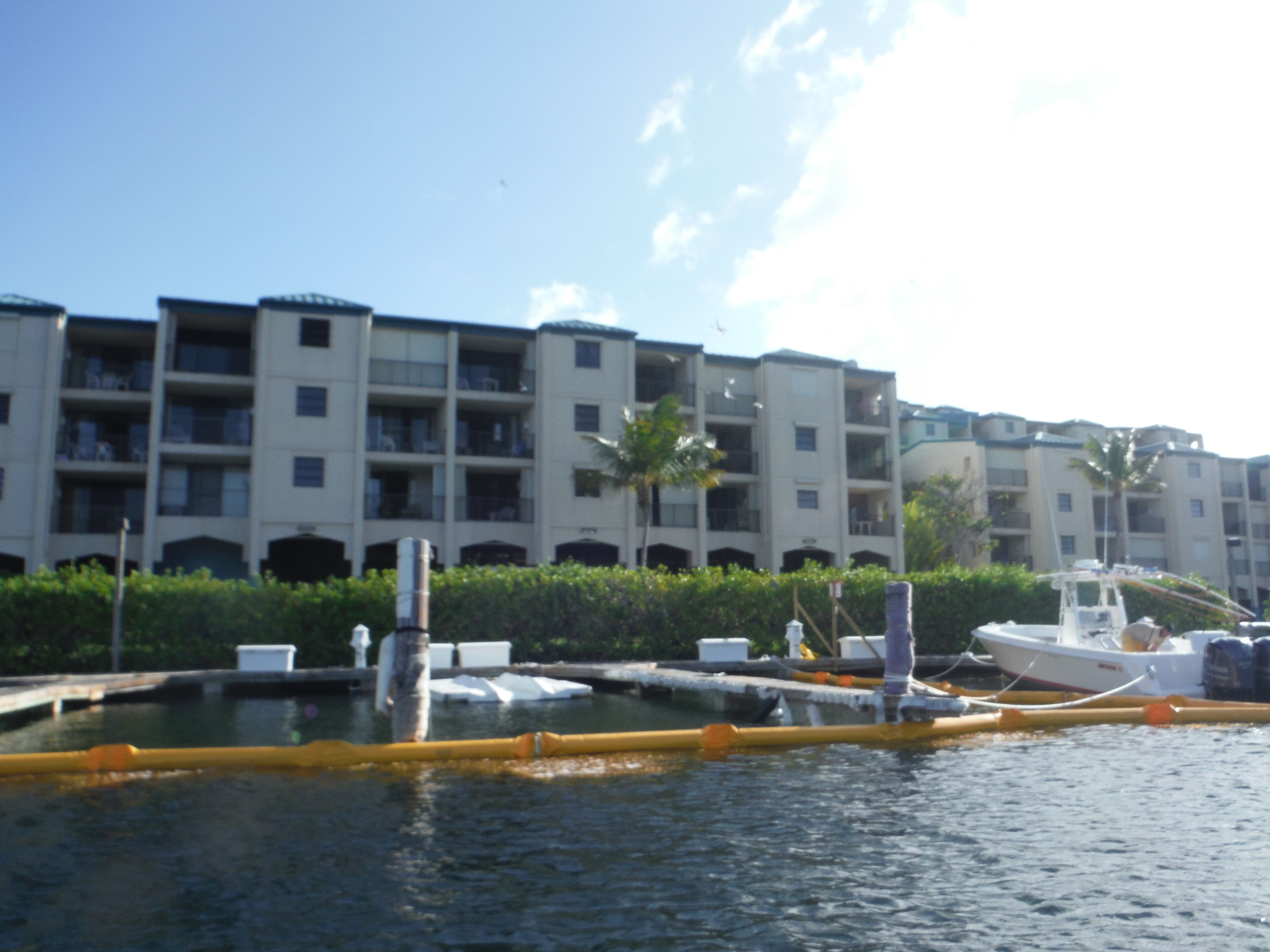 A marina with a white boat docked, surrounded by a building with multiple balconies and a clear blue sky.