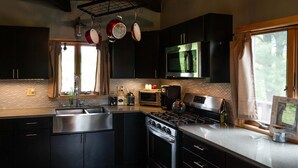 Une cuisine moderne avec des meubles de couleur sombre, des appareils en acier inoxydable, un grand îlot central et une fenêtre avec des rideaux.