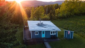 Une maison avec une terrasse, une cheminée et un petit abri de jardin.
