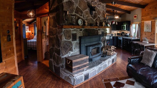 L’intérieur chaleureux d’un chalet avec une cheminée en pierre, un canapé en cuir, un plancher en bois et un coin cuisine.