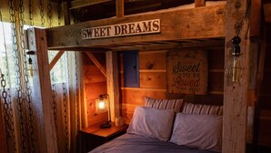 Une chambre confortable, aménagée dans une cabane en bois, avec un lit, des oreillers, une table de chevet, une lampe et un panneau sur lequel on peut lire : « Faites de beaux rêves ».