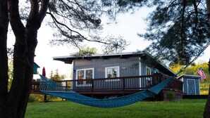 Une maison avec une terrasse, un hamac et un petit abri de jardin orné d’un drapeau américain.