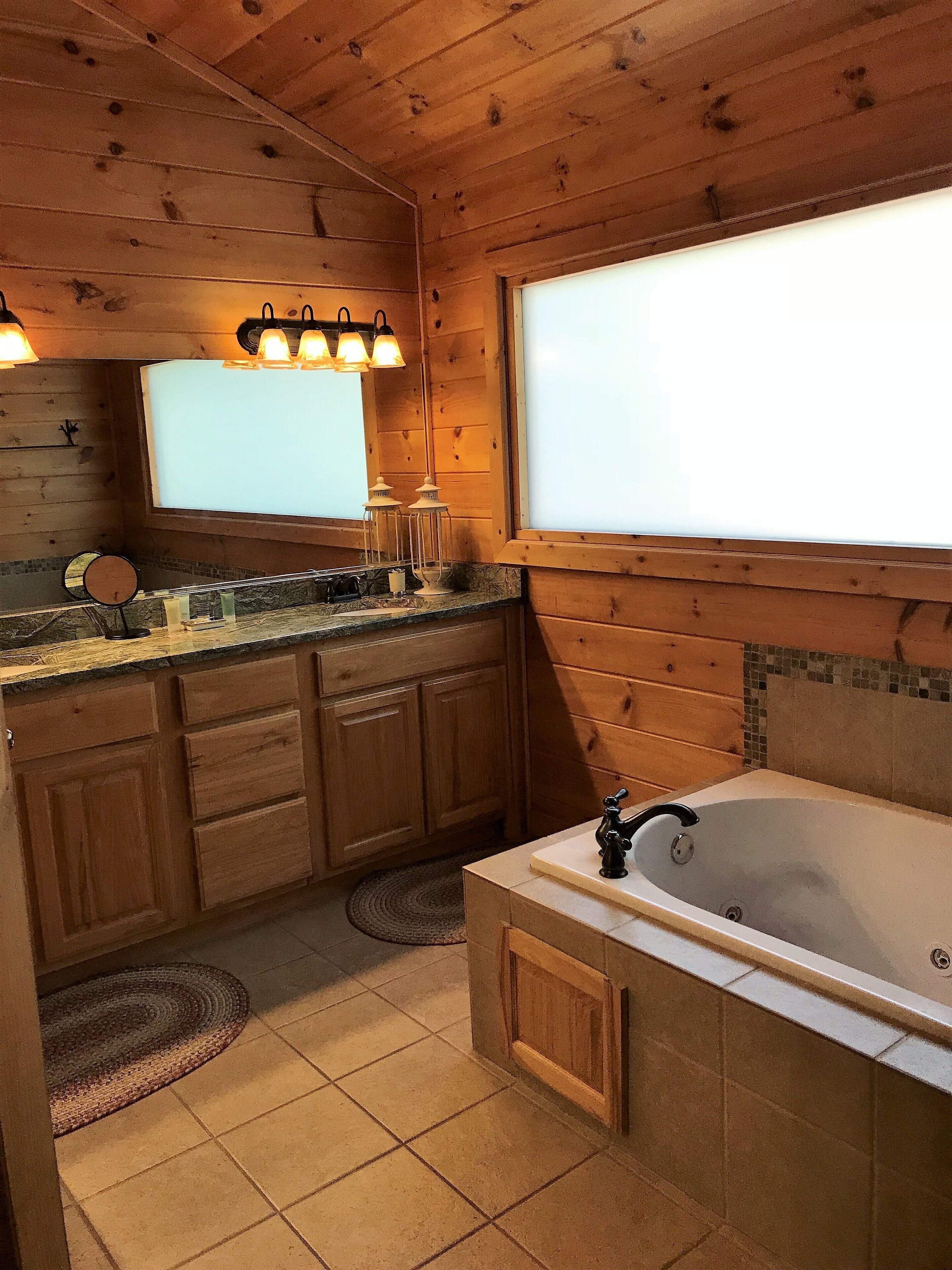 Une salle de bain rustique, aménagée dans une cabane en bois, avec une grande fenêtre, un lavabo et une baignoire.