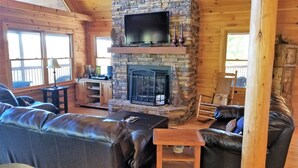 A cozy cabin interior with a stone fireplace, leather sofas, and a television mounted above it. - Long Range Views! 3 Fireplaces-Sleeps 20-Blue Ridge-Pool Table/HotTub-Pets OK. (Blue Ridge)