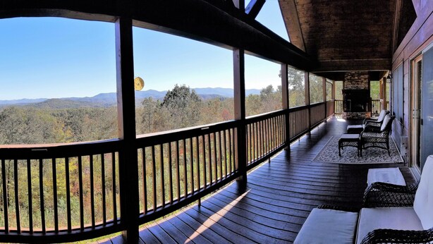 A covered porch with a stone fireplace, wooden railing, and outdoor seating. - Long Range Views! 3 Fireplaces-Sleeps 20-Blue Ridge-Pool Table/HotTub-Pets OK. (Blue Ridge)