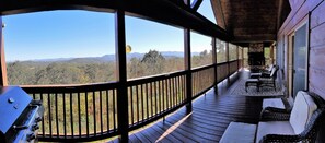 Une véranda couverte avec une cheminée en pierre, une balustrade en bois et des sièges d’extérieur.