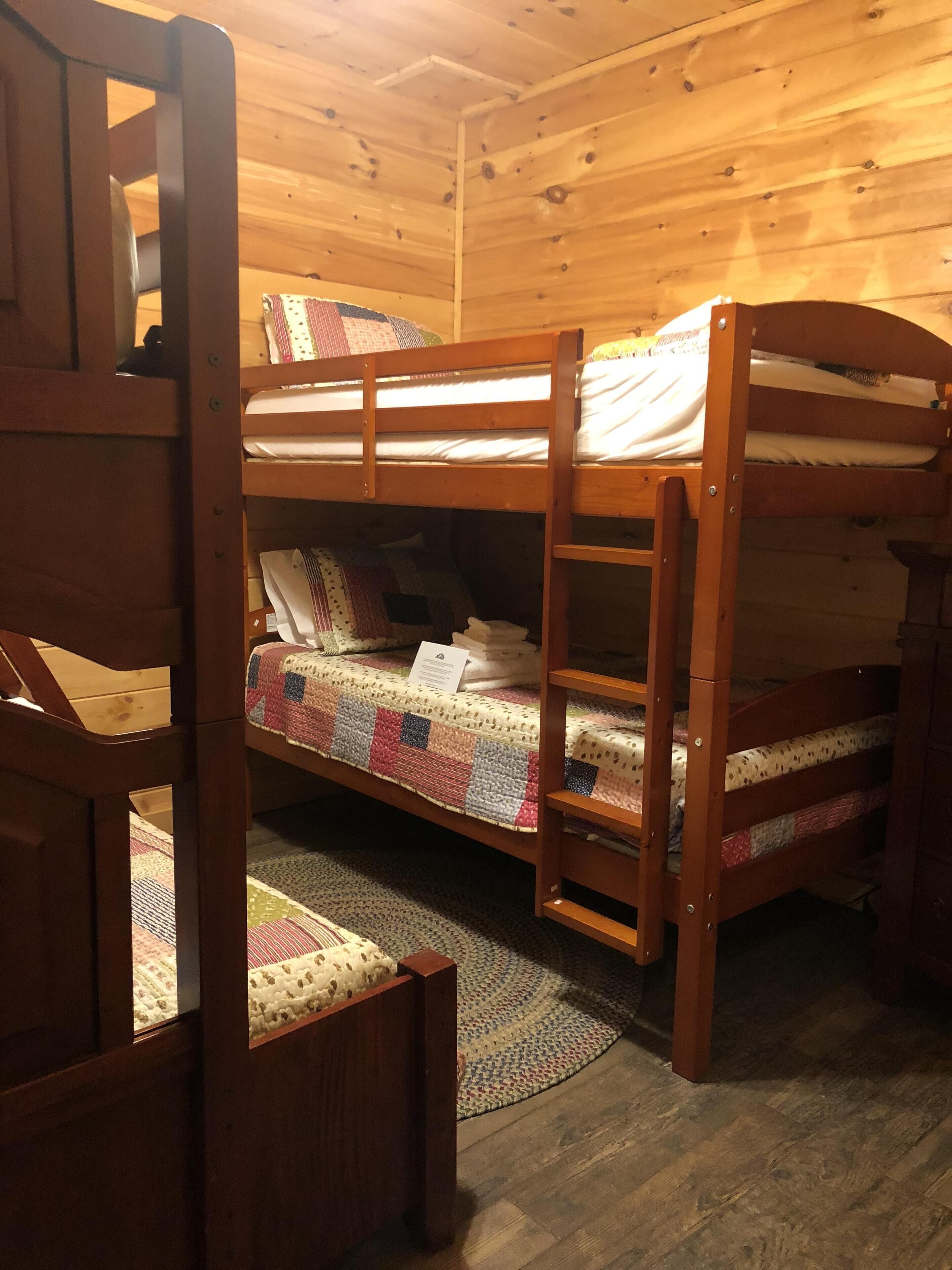 A bunk bed room with wooden walls and floors, a small rug, and a quilted bedspread.