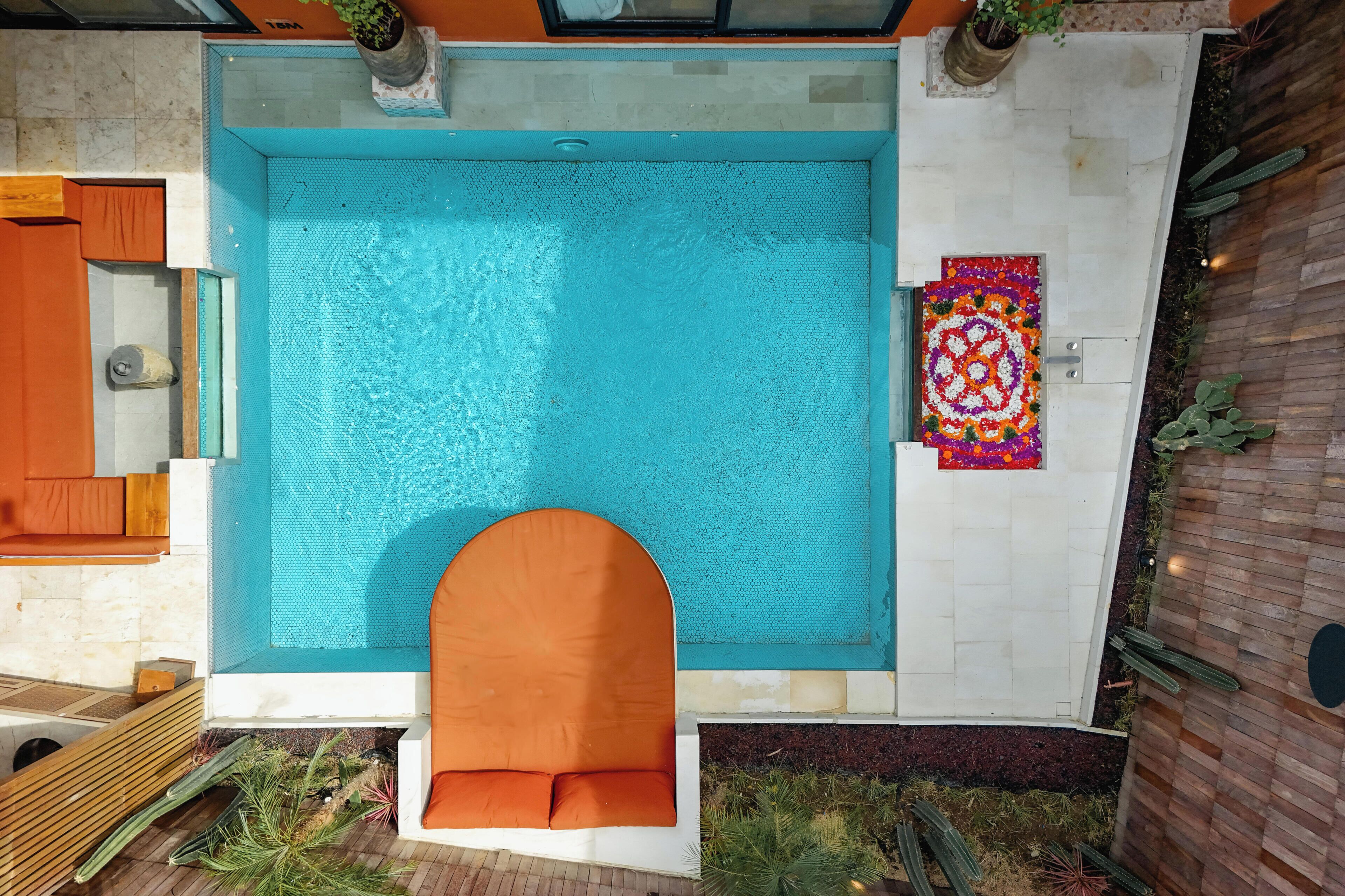 A rooftop pool with a wooden deck, a seating area, and a colorful decorative rug.