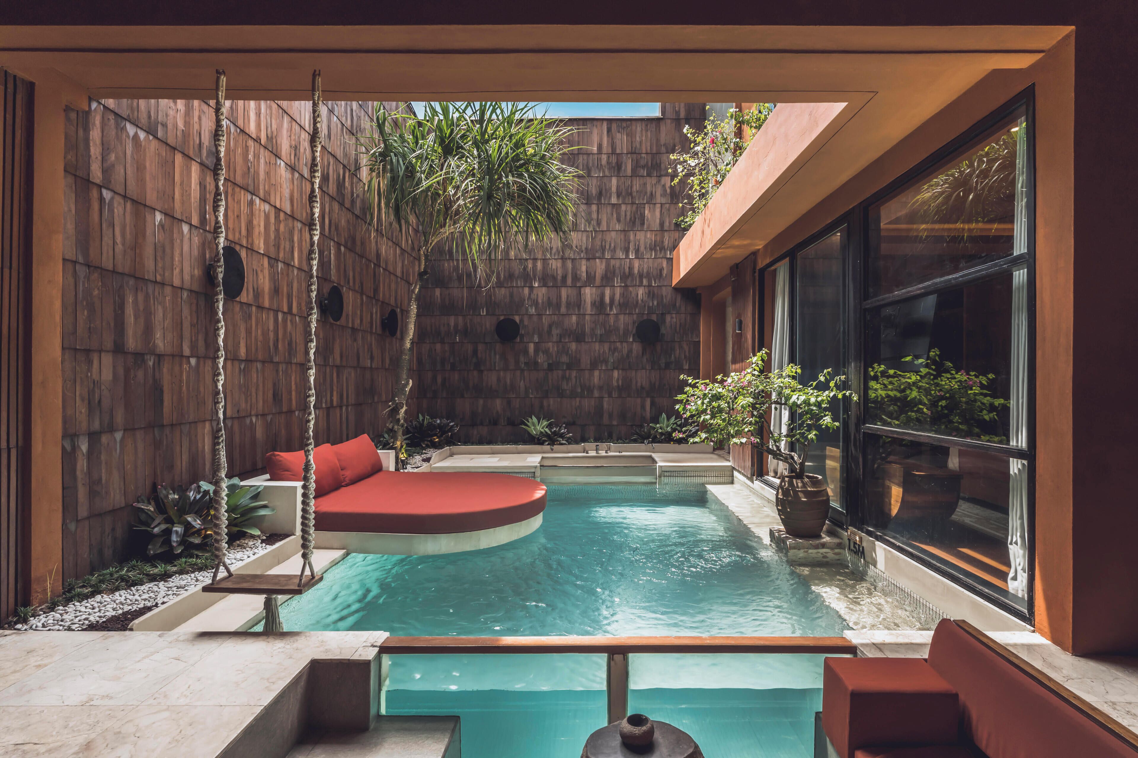 A modern outdoor pool area with a swing chair, seating, and a view of the surrounding garden.
