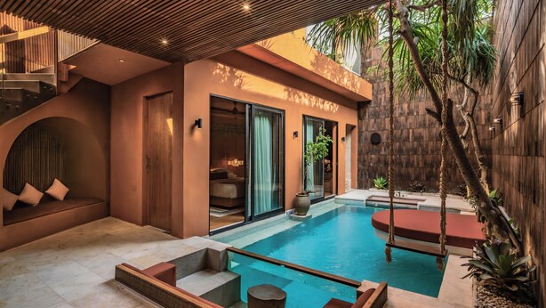 A modern outdoor pool area with a wooden deck, a seating area with cushions, and a staircase leading to an upper level. - Sana Vie Villa Seminyak by Ini Vie Hospitality (Seminyak)