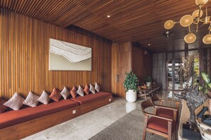 Et moderne interiør med en væg af træpaneler, en rød sofa med mønstrede puder, en stor stueplante og et spiseområde med træstole og et bord.