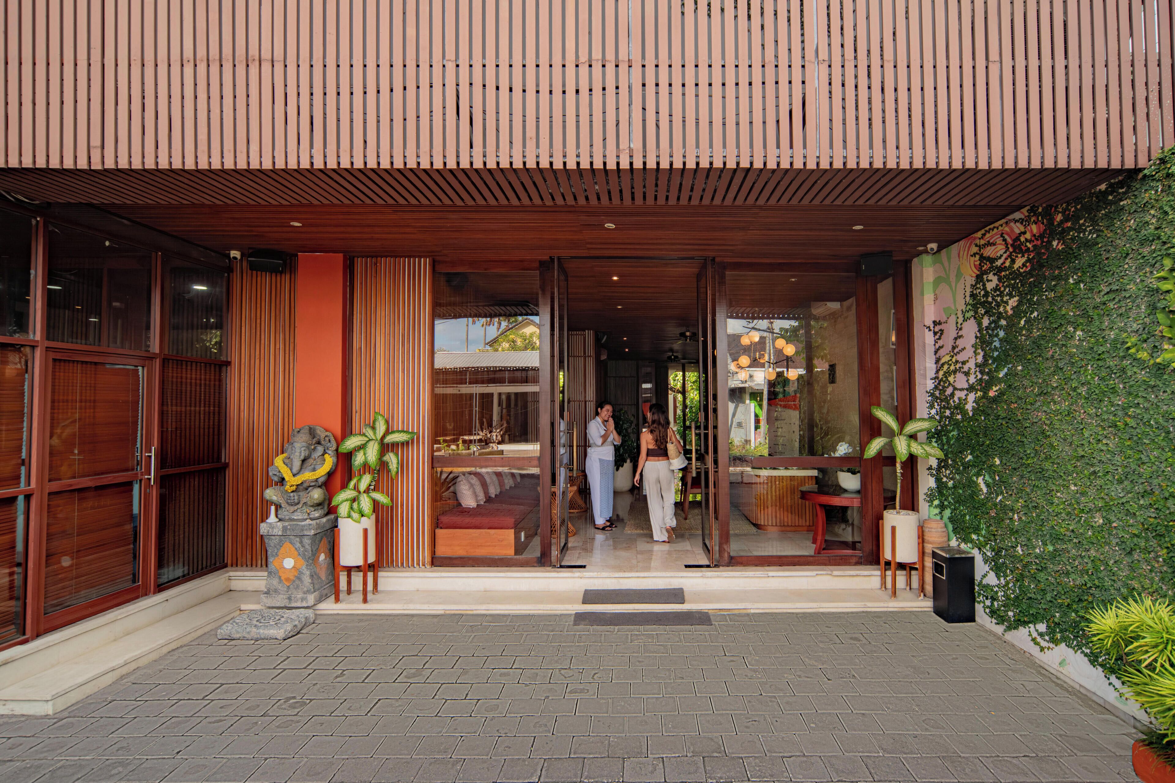 A building entrance with a wooden slatted roof, a glass door, and a paved walkway.