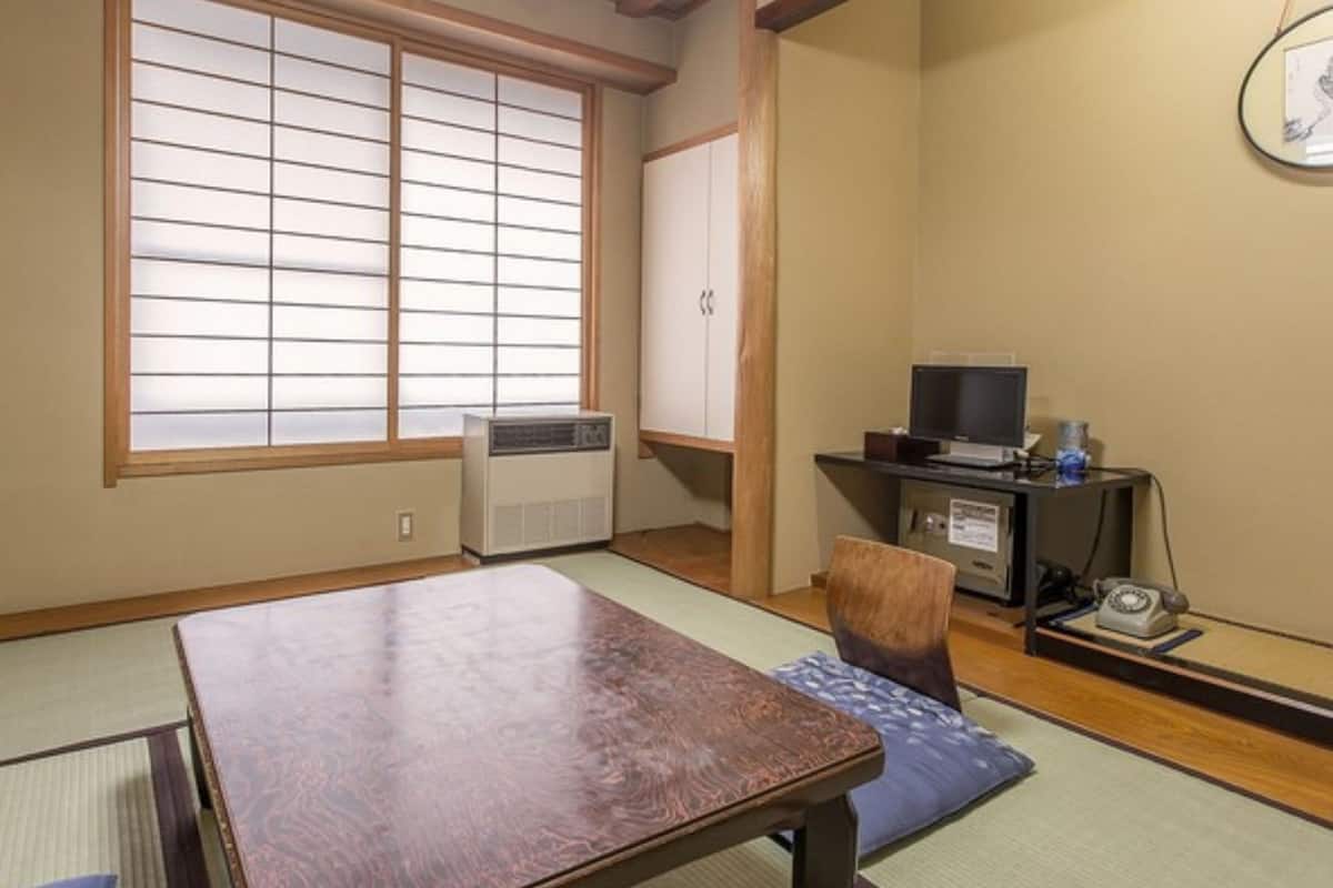 Ein traditioneller japanischer Raum mit Tatami-Böden, einem niedrigen Tisch, einem Fernseher auf einem Standfuß und einem Heizgerät.