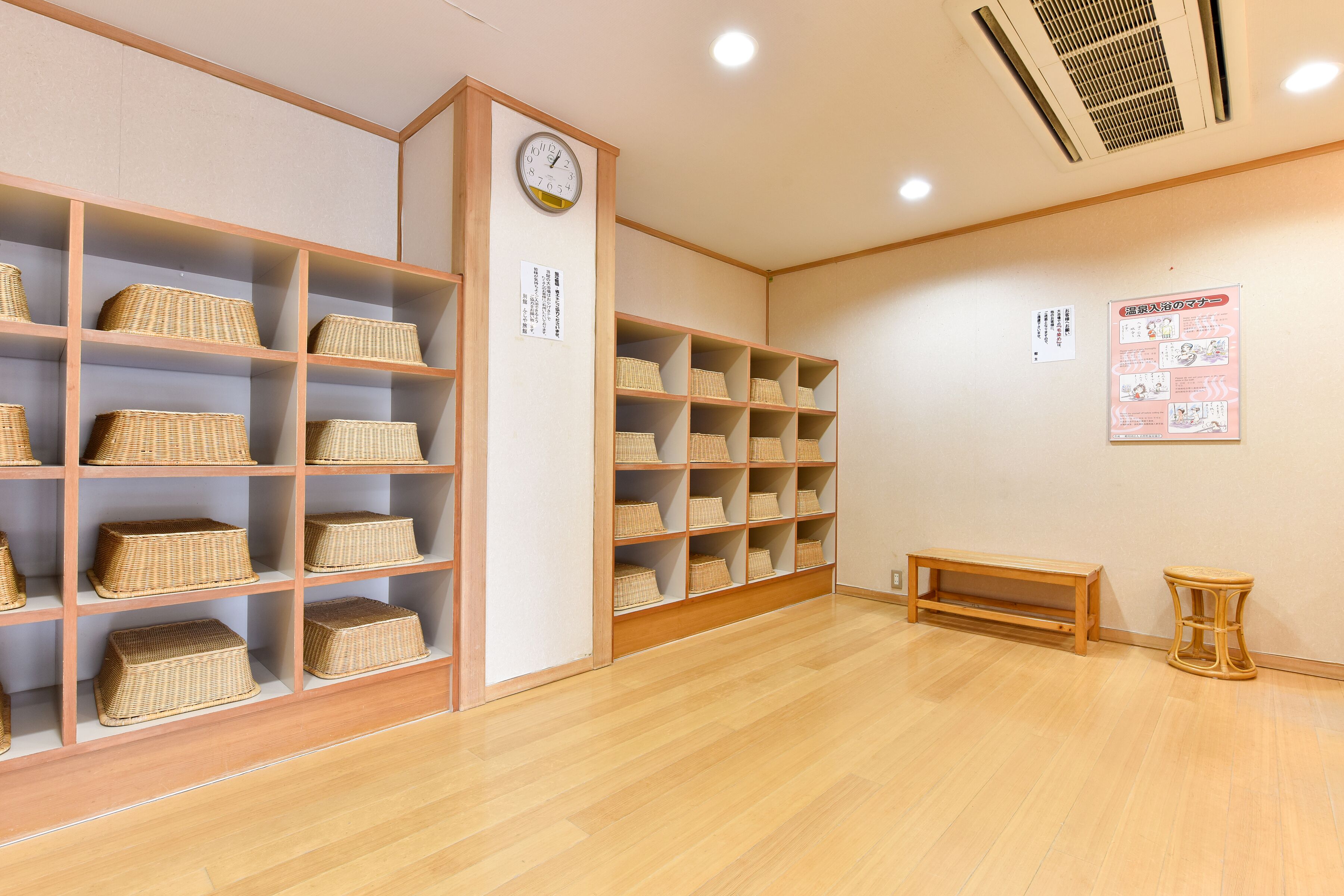 Una habitación con estanterías de madera que contienen cestas de mimbre, un banco de madera y un taburete pequeño.