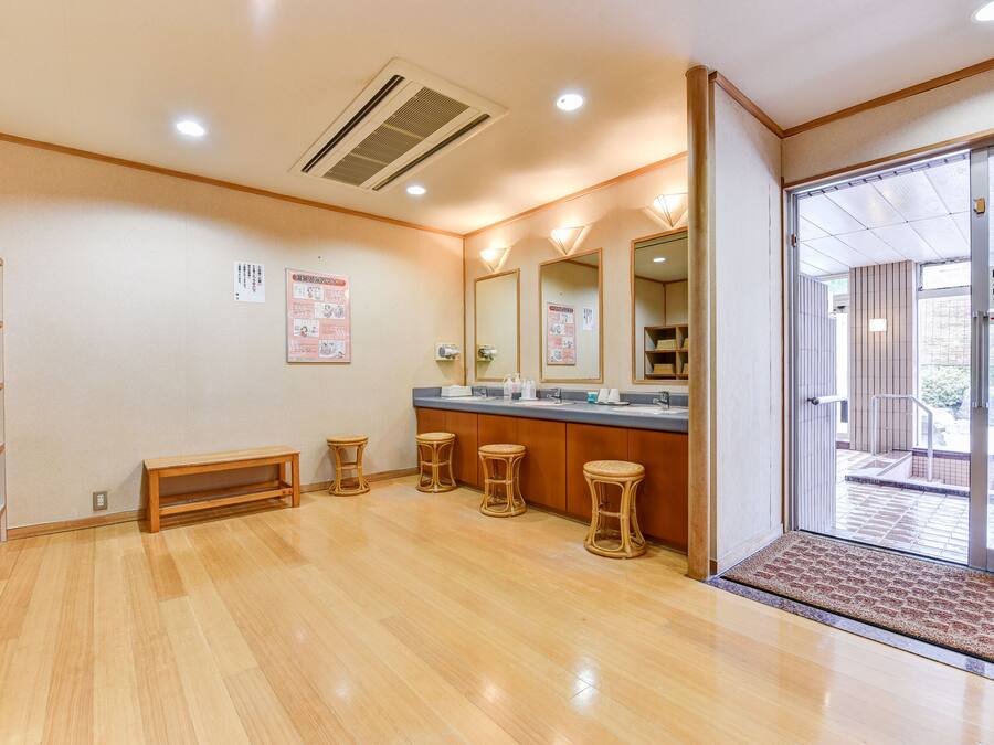 A clean, modern bathroom with wooden flooring, a bench, and a counter with stools.