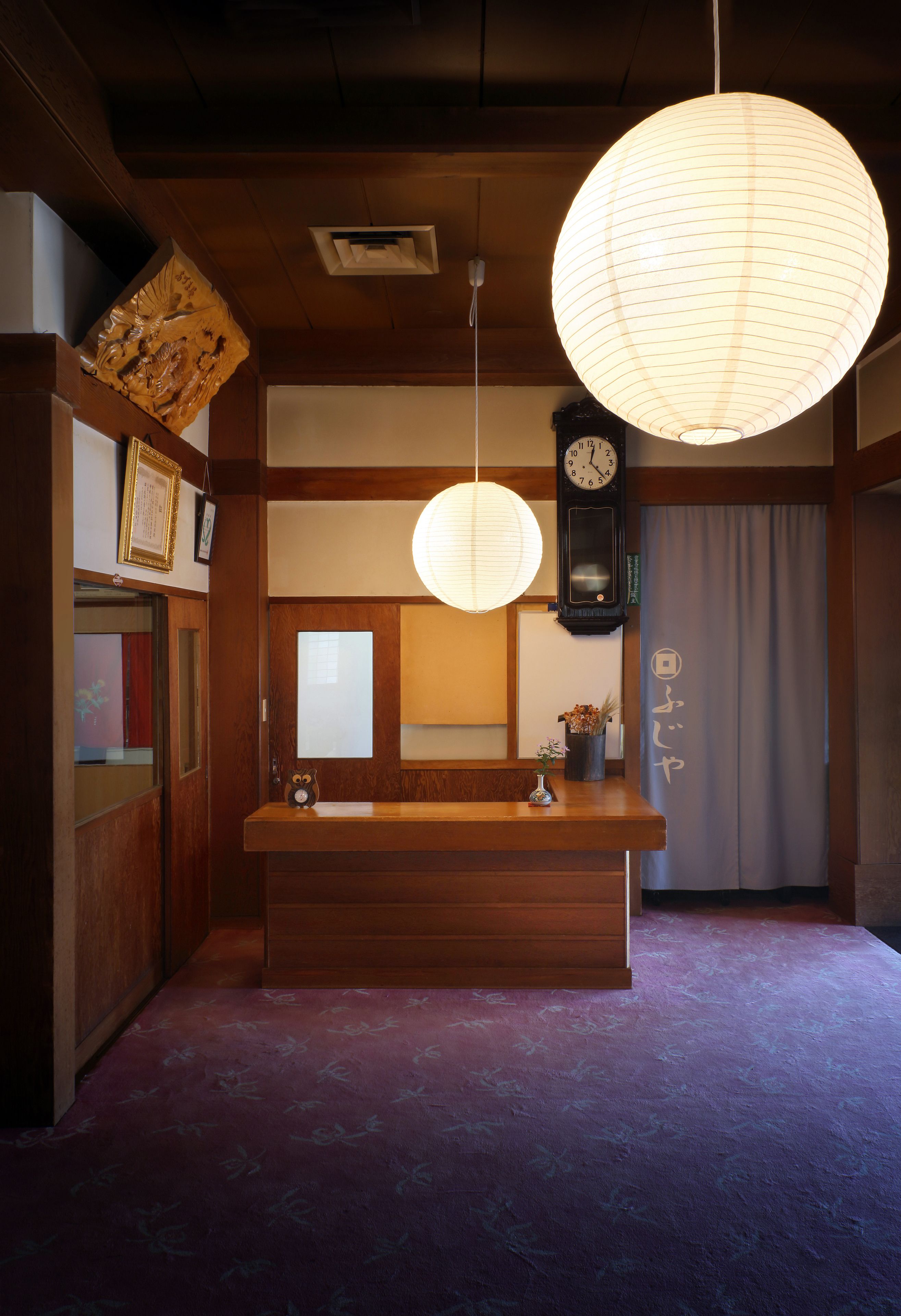 Ein traditionelles japanisches Interieur mit einem hölzernen Empfangstresen, einer hängenden Papierlaterne und einer Wanduhr.