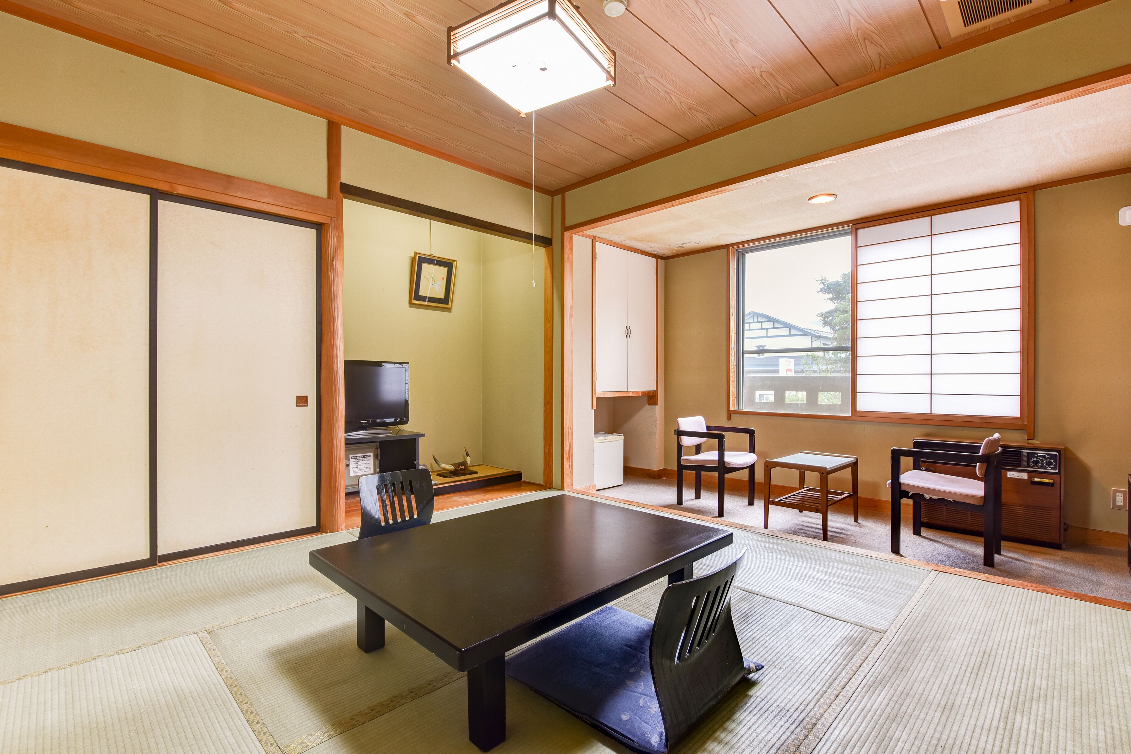 Una habitación japonesa tradicional con suelo de tatami, una mesa baja, un televisor y puertas correderas.