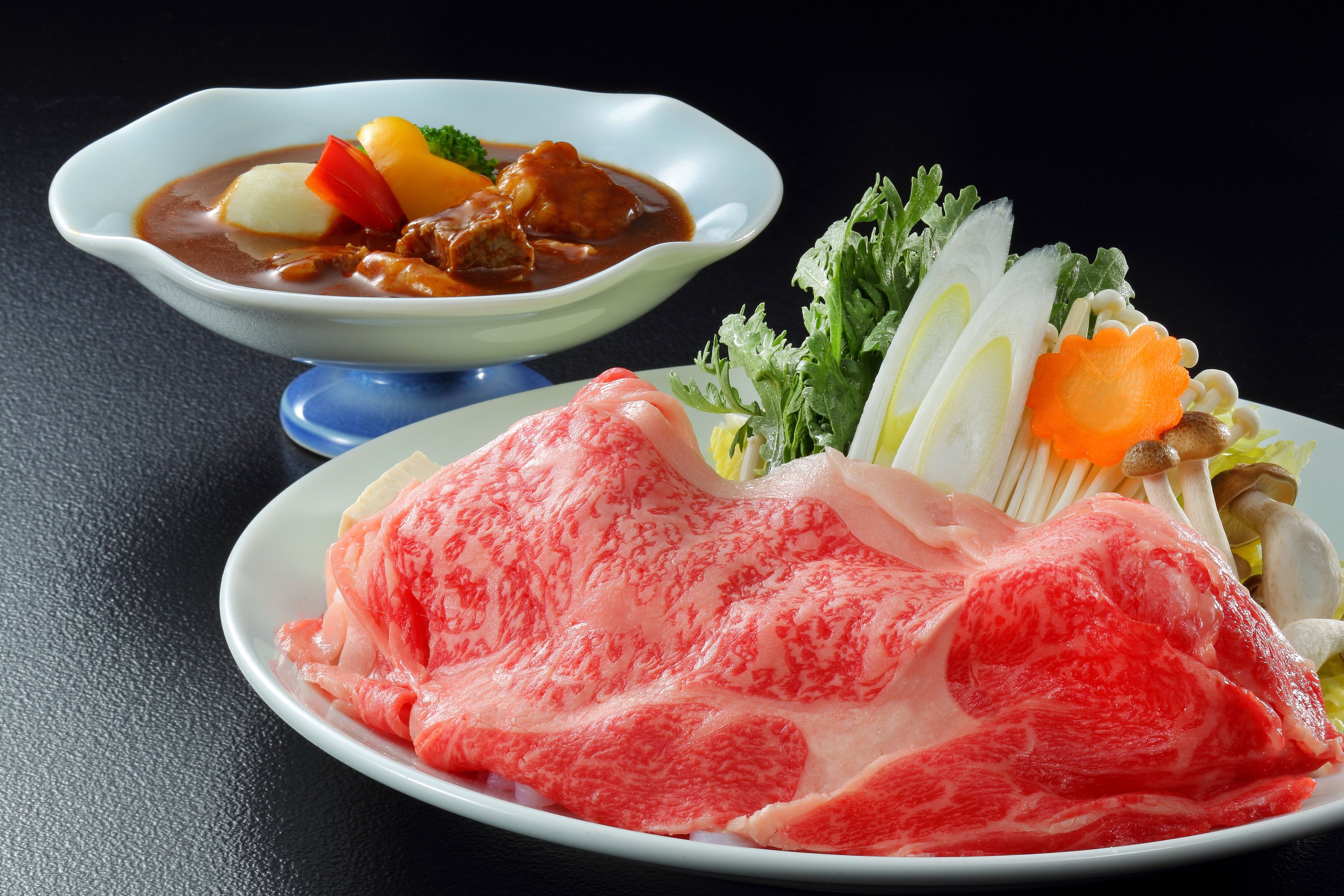 A plate of raw meat and a bowl of stew with vegetables.