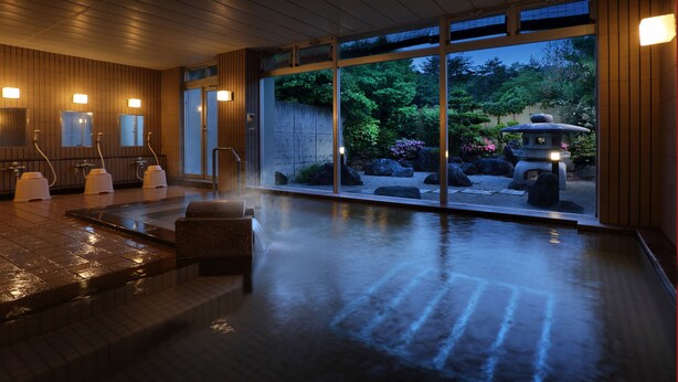 A traditional Japanese onsen with wooden interiors, a stone hot spring, and a view of a garden with rocks and a pagoda. - Bekkan Fujiya Ryokan (Kaminoyama)
