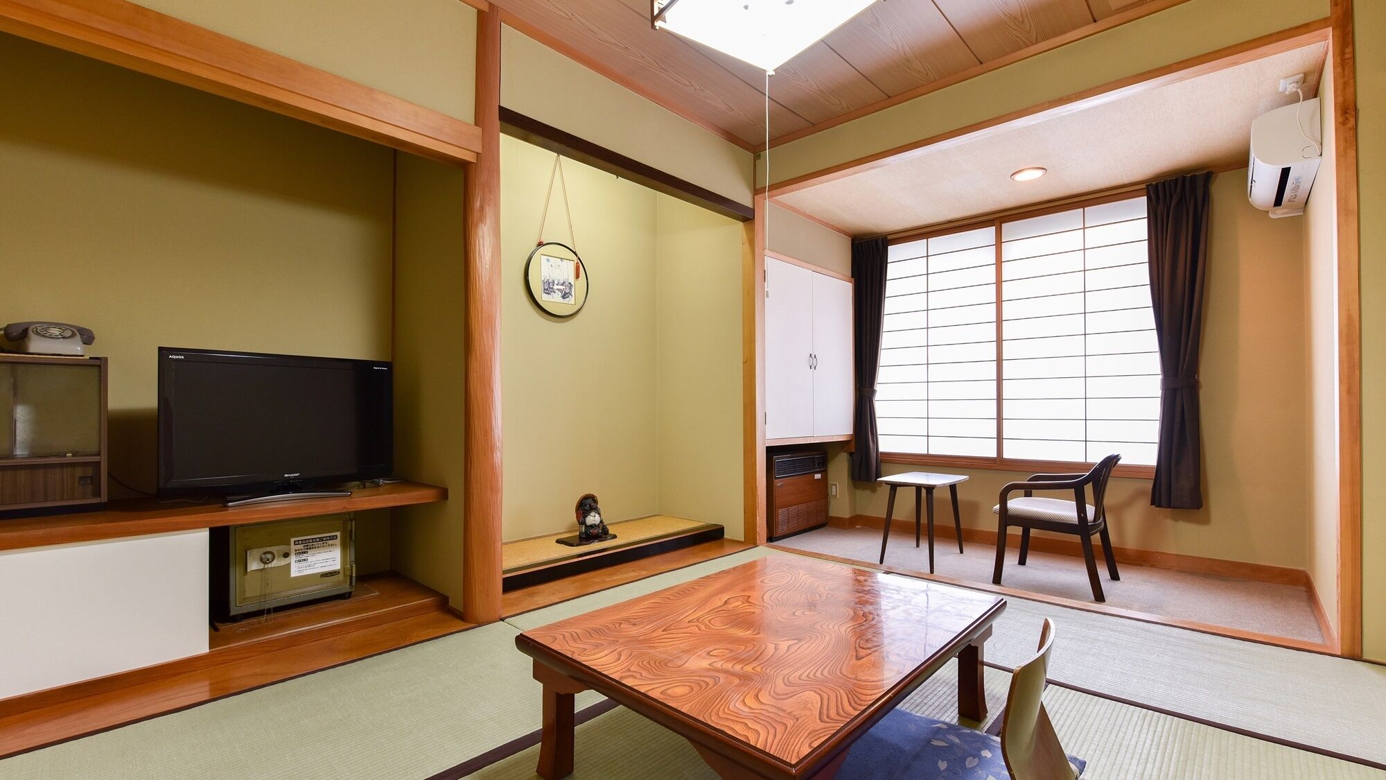 Um quarto japonês tradicional com tatames, uma televisão, um pequeno santuário, uma porta deslizante e vista para o exterior.
