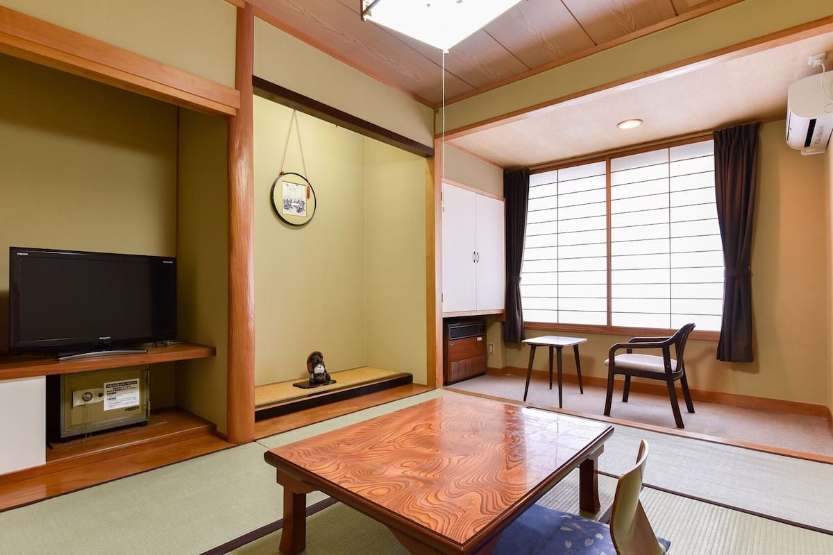 Um quarto japonês tradicional com tatames, uma televisão, um pequeno santuário, uma porta deslizante e vista para o exterior.