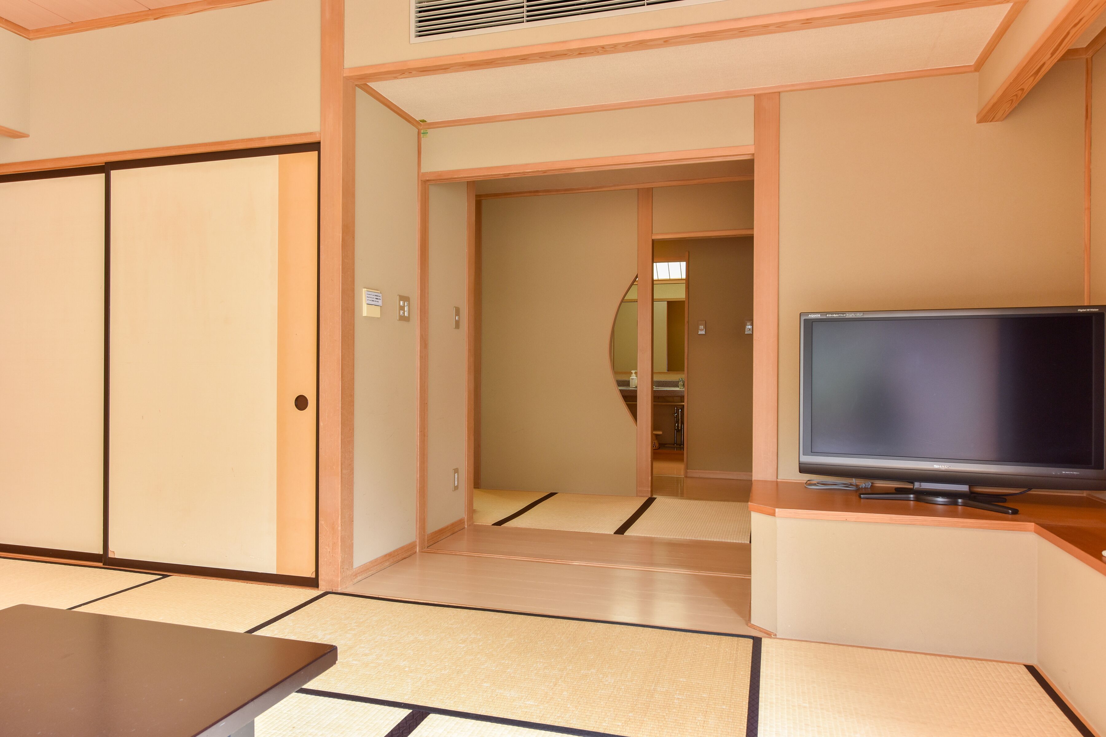 Una habitación japonesa tradicional con suelo de tatami, un televisor sobre un soporte de madera y puertas correderas.