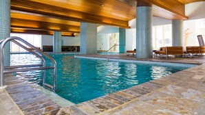 Una piscina interior con techo de madera, paredes de azulejos y suelo de piedra.