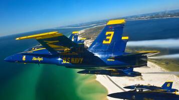 Un avión de los Blue Angels de la Marina estadounidense, con el número 3, volando sobre una playa con cielos despejados.