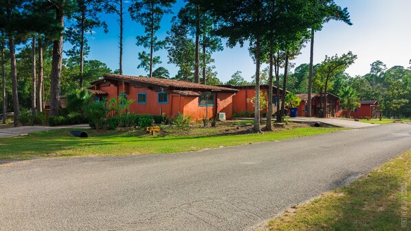 Un bâtiment rouge avec un toit en tuiles, entouré d’arbres et bordé d’une allée gravillonnée.