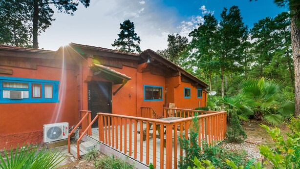 Een houten huis met veranda, omringd door weelderige begroeiing en bomen.