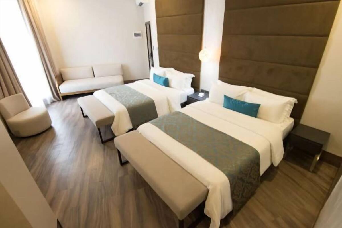 A hotel room with two beds, a sofa, a bench, and a nightstand.