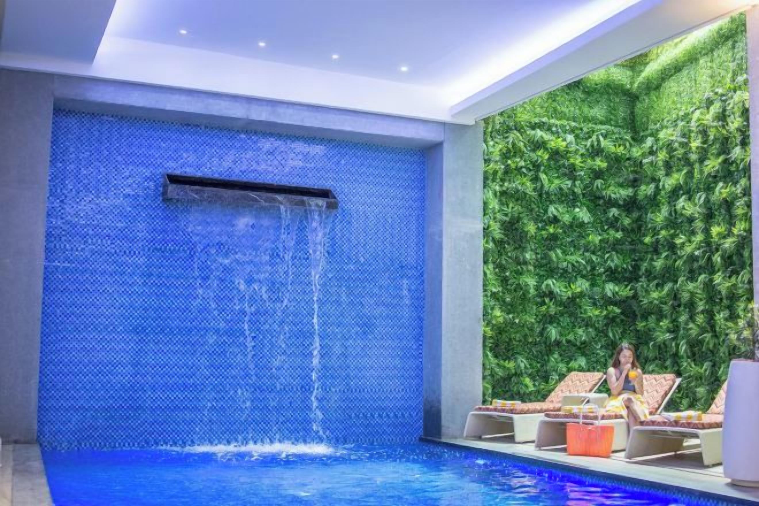 A modern indoor pool area with a blue mosaic wall and a waterfall feature.