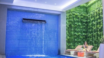 A modern indoor pool area with a blue mosaic wall and a waterfall feature.