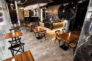 Interior de un restaurante con suelo de mármol, mesas y sillas de madera, una zona de bar central y una lámpara moderna.