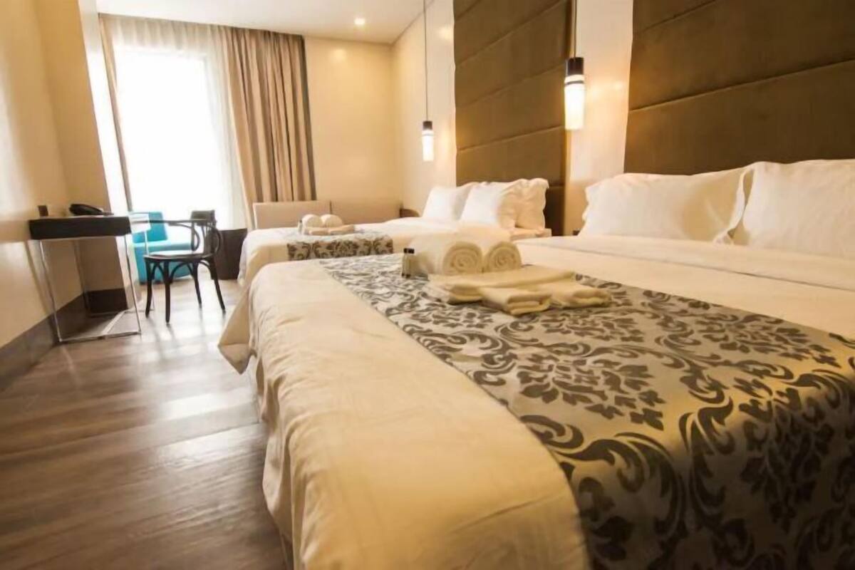 A hotel room with a large bed, a desk with a chair, and a window with curtains.