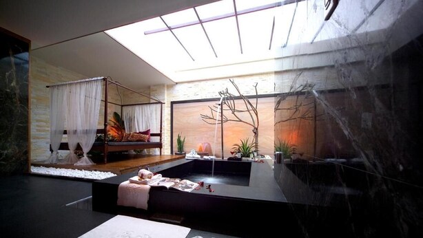 Un spa moderno con techo de vidrio, una bañera de hidromasaje y un banco de madera con cojines.