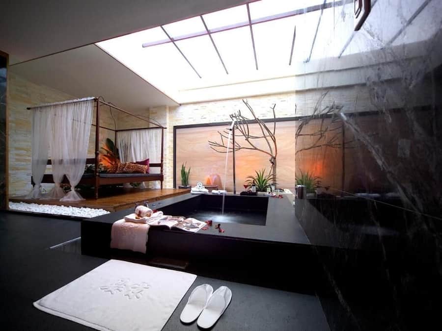 Um spa moderno com teto de vidro, uma banheira de hidromassagem e um banco de madeira com almofadas.