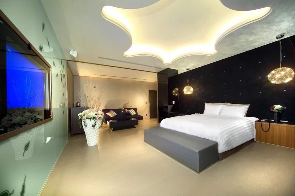 A modern bedroom with a large bed, a seating area with a sofa, a decorative vase, and a unique ceiling light fixture.