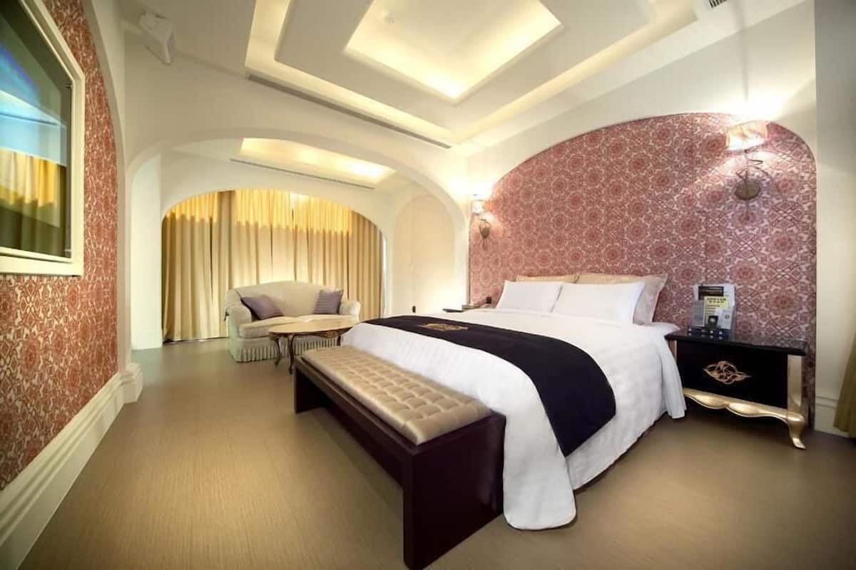 A hotel room with a large bed, a bench, a small table, and a nightstand.