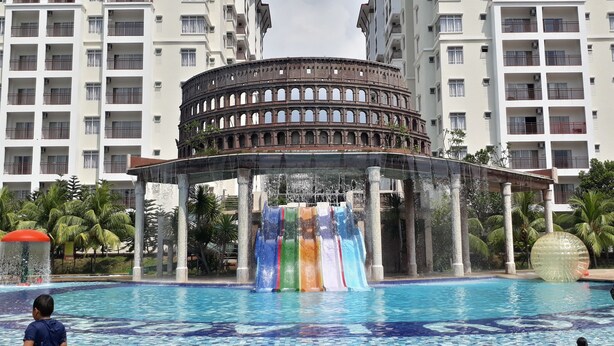 A swimming pool with a Roman-style fountain structure in the center, surrounded by modern apartment buildings. - Junikastay Blagoon Melaka (Malacca City)