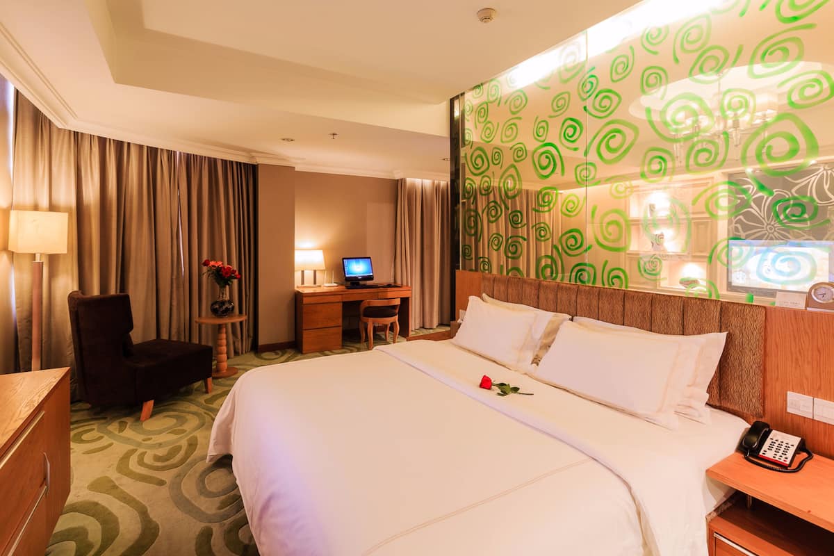 A hotel room with a large bed, a desk with a computer, a chair, and a telephone.